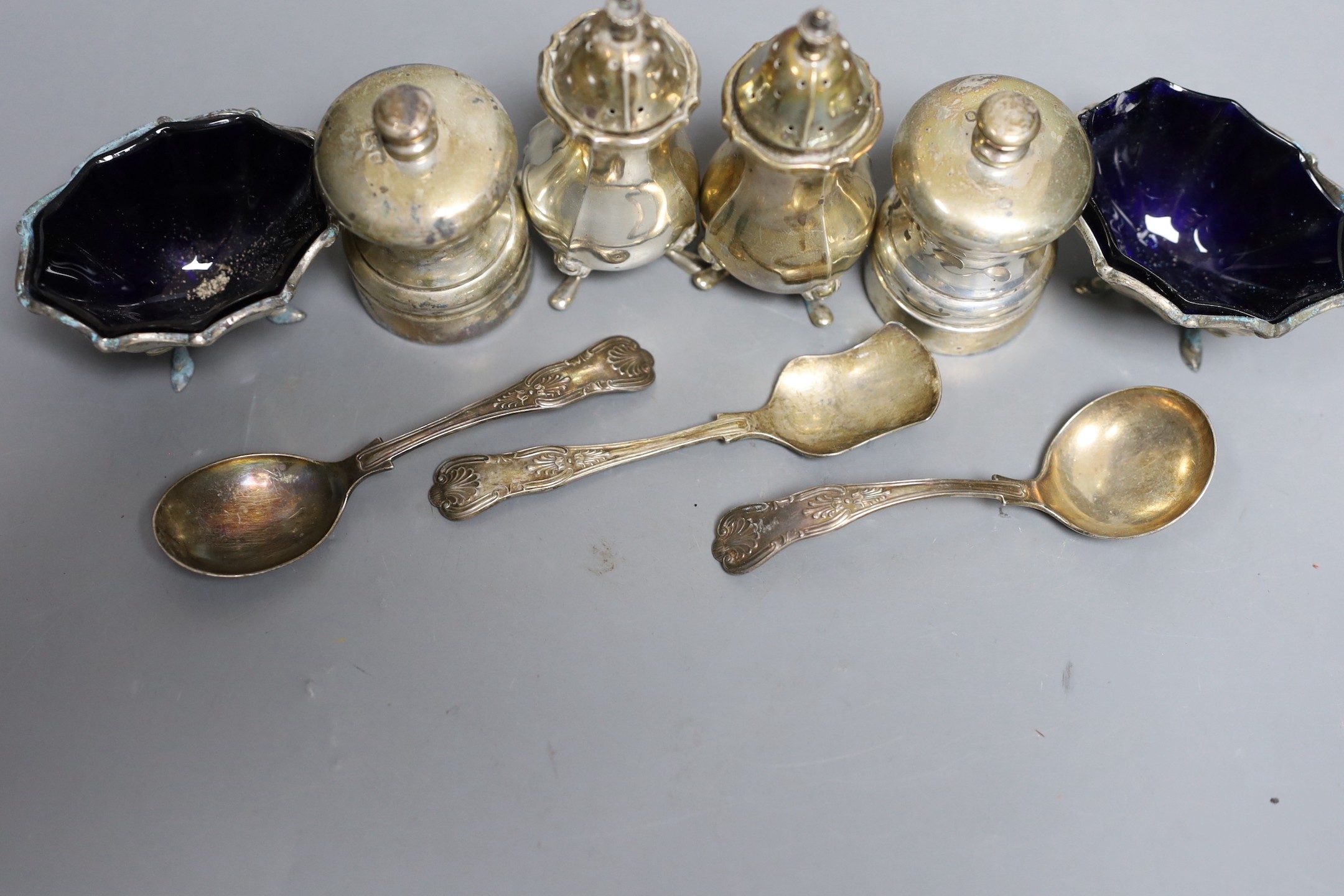 A modern pair of silver capstan shaped pepper mills, a pair of silver salts and pepper pots, a pair of matching salts and three various spoons.